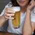 Eine Frau in München in weißem T-Shirt hält ein Glas Bier in der Hand.