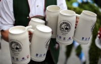 Ein Mann in Tracht tr&auml;gt in jeder Hand drei gef&uuml;llte Steinma&szlig;kr&uuml;ge auf dem Brauertag in M&uuml;nchen.