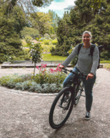 Eine Frau h&auml;lt mit ihrem Moutainbike in einer Gartenanlage an.