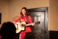 Die Kabarettistin Claudia Pichler steht auf einer B&uuml;hne und spielt auf einer Gitarre.