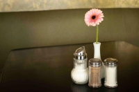 On a table in Caf&eacute; Jasmin in Munich, a pink gerbera stands in a vase next to salt, sugar and pepper shakers.