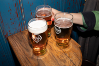 Drei Biergl&auml;ser auf einem Holztisch und eine Person greift danach.