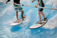Zwei Surfer stehen auf Surfboards auf einer k&uuml;nstlichen Surfwelle.