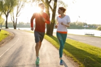 A woman and a man are jogging through the Olympic Park in Munich in the evening sun.