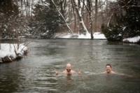 Dw&oacute;ch mężczyzn pływa zimą w Eisbach w Monachium. Na brzegu leży śnieg.
