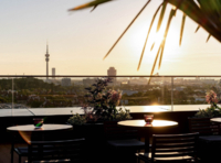 Blick von der Muniqo Dachterrasse auf den Olympiapark bei Sonnenuntergang.