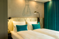 Doppelbett in einem Hotelzimmer in M&uuml;nchen mit gr&uuml;nen und wei&szlig;en Kissen.