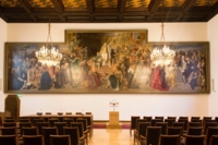 Blick auf ein gro&szlig;es Gem&auml;lde in einem Sitzungssaal im Neuen Rathaus in M&uuml;nchen. Davor h&auml;ngen zwei Kronleuchter.