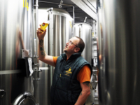 Steffen Marx, der Gr&uuml;nder von Giesinger Br&auml;u in M&uuml;nchen, steht vor einem Braukessel und pr&uuml;ft ein Glas Bier.