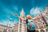Eine Frau steht mit einem Rucksack vor dem Rathaus in M&uuml;nchen.