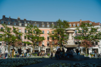 Personen stehen und sitzen am G&auml;rtnerplatz in M&uuml;nchen bei Sonnenschein.