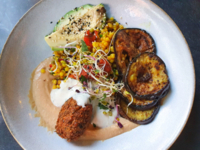 A plate of fried aubergine, corn, avocado and other vegetarian food.