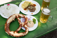 View of a green table in a beer garden in Munich with two beer glasses, pretzels, obazden and radish.