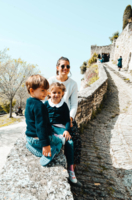 Carina and her children sit on a stone wall in the sunshine.