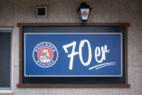 A house wall with a blue sign saying "70er" and the "Paulaner" sign in Munich.