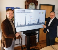 Dr. Christian Scharpf und Benedikt Brandmeier stehen vor einer Pr&auml;sentation &uuml;ber den M&uuml;nchner Hotelmarkt 2025.