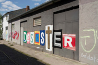 Auf die Au&szlig;enwand eines Schuppens steht mit verschiedenfarbige Buchstaben das Wort "Desaster"  geschrieben.