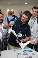 Ein Mann zeigt Besucher*innen auf dem ISAKOS Kongress medizinisches Werkzeug an einem Roboter.
