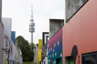 Bunte Bungalows im Olympischen Dorf M&uuml;nchen mit dem Olympiaturm im Hintergrund