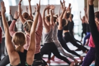 Mehrere Personen machen Yoga und strecken Ihre Arme in die H&ouml;he.