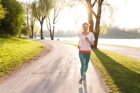 Eine Frau joggt in der Abendsonne durch den Olympiapark in M&uuml;nchen.