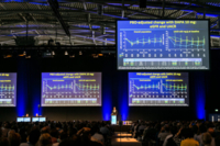 Blick in abgedunkelte Kongresshalle auf das Podium und blau leuchtende Screens