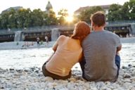 Ein Paar sitzt, dem Wasser zugewandt, an der Isar in München.