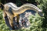 A view from above of a large replica of a dinosaur and a family standing next to it, looking up.
