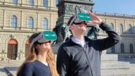 Gäste des TimeRide tragen eine VR Brille vor der Residenz in München.