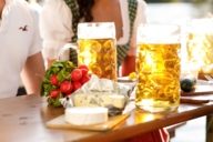 Zwei Masskrüge mit Bier und einem Bündel Radieschen auf einem Tisch in einem Münchner Biergarten.