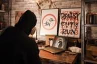 Ein Mann in schwarzem Hoodie von hinten, der auf einen Laptop und Kunstwerke von Banksy schaut.