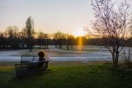 Eine Frau sitzt auf einer Bank in der winterlichen Abendsonne im Olympiapark in München