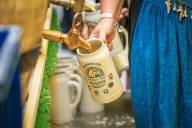 Close-up of a beer barrel being tapped into a stone mug by a woman wearing a blue dirndl apron at the 2022 Brewers' Day.