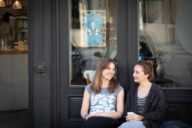 Stephanie Bjarnason und Anika Landsteiner sitzen vor einem Café.