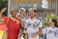 Eine Gruppe von Fußballfans, darunter zwei Frauen und zwei Männer in den Trikots der deutschen und spanischen Nationalmannschaft feiern in der Münchner Fußgängerzone.