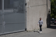 Ein Mann mit Sonnenbrille läuft entlang einer Mauer in München und lacht.