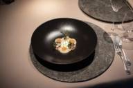 Im Restaurant Atelier im Bayerischen Hof steht ein schwarzer Teller mit einem Gericht auf dem Tisch