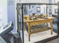 Holztisch mit zahlreichen Laborgeräten in einer Glasvitrine.
