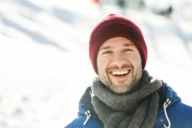 Ein Mann mit roter Mütze lächelt an einem Wintertag in München in die Kamera.