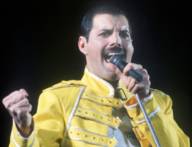 Freddie Mercury singt am Mikrofon und trägt ein gelbes Outfit.