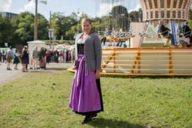 Frau auf dem Oktoberfest in München steht in Tracht vor einem Kettenkarussell.