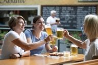 Drei Touristinnen prosten sich mit Bierkrügen zu.