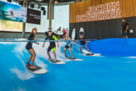 Vier Personen surfen in der Jochen Schweizer Arena in München auf einer stehenden Welle.