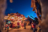 Ein bunt beleuchtetes nostalgisches Kinderkarussell vor blauem Nachthimmel mit Kindern und Erwachsenen als Fahrg&auml;sten darin.