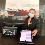 Eine Rezeptionistin steht mit einem Tablet im Hotel Hilton Munich Airport.