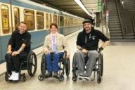 Zwei Rollstuhlfahrer und eine Rollstuhlfahrerin vor einer Münchner U-Bahn am Bahnsteig