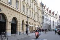 Eine Frau und ein Mann fahren auf einem roten Roller durch die M&uuml;nchner Altstadt