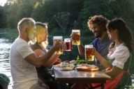 Eine Gruppe von Menschen sitzt abends an einem Tisch in einem Biergarten in München und prostet sich zu.
