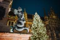 Eine Statue vor dem Rathaus und einem beleuchtenden Weihnachtsbaum auf dem Christkindlmarkt am Marienplatz in München