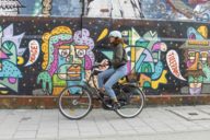 Frau auf einem Fahrrad vor einer Mauer mit Graffiti in München.